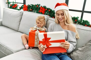 Mother and daughter unboxing gift sitting by christmas decor at home