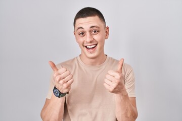 Young man standing over isolated background success sign doing positive gesture with hand, thumbs up smiling and happy. cheerful expression and winner gesture.