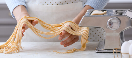 Woman making pasta with machine in kitchen, closeup