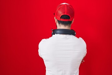 Hispanic man with beard wearing gamer hat and headphones standing backwards looking away with...