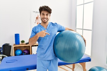 Hispanic physiotherapy man working at pain recovery clinic smiling happy pointing with hand and finger