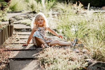 Portrait of poor crying awesome little girl with long fluffy curly hair wearing dress with stars, sitting after falling.