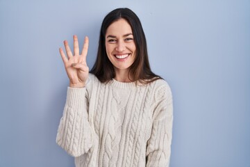 Young brunette woman standing over blue background showing and pointing up with fingers number four while smiling confident and happy.