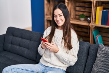 Young woman using smartphone sitting on sofa at home
