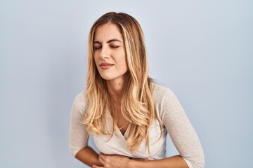 Fototapeta premium Young blonde woman standing over isolated background with hand on stomach because indigestion, painful illness feeling unwell. ache concept.