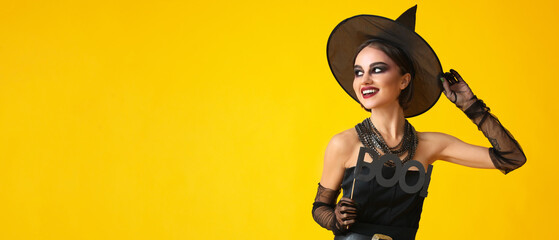 Beautiful young woman in Halloween costume of witch on yellow background with space for text