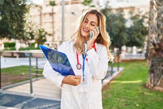 Young blonde woman wearing doctor uniform talking on the smartphone at park