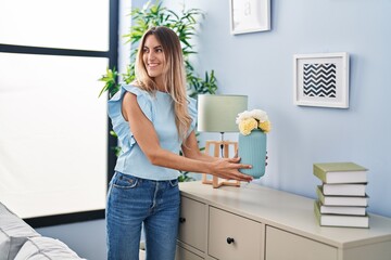 Young woman smiling confident holding plant pot at home