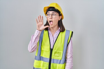 Hispanic girl wearing builder uniform and hardhat shouting and screaming loud to side with hand on mouth. communication concept.