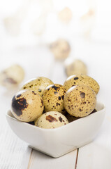 Quail eggs in square bowl on wooden plank table.