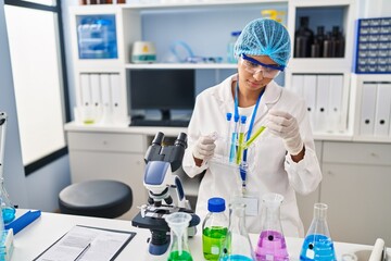 Fototapeta premium Young latin woman wearing scientist uniform holding test tubes at laboratory