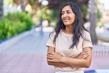 Young beautiful hispanic woman standing with arms crossed gesture at park