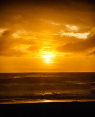 paisaje de ocaso en la playa con silueta del sol sobre el mar con olas reventando en la orilla con cielo anaranjado