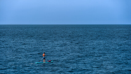 One man practicing paddle board or paddle surfing on a sunny day in the middle of the sea