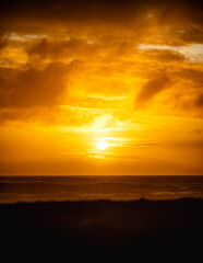 Naklejka na ściany i meble paisaje de ocaso en la playa con silueta del sol sobre el mar con olas reventando en la orilla con cielo anaranjado