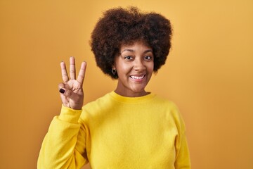 Young african american woman standing over yellow background showing and pointing up with fingers...