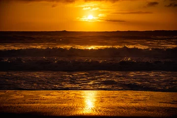 Poster paisaje de ocaso en la playa con silueta del sol sobre el mar con olas reventando en la orilla con cielo anaranjado © Richard