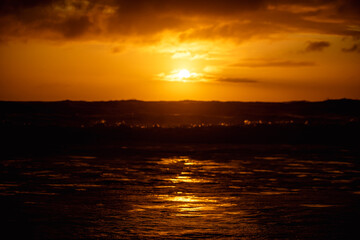 paisaje de ocaso en la playa con silueta del sol sobre el mar con olas reventando en la orilla con cielo anaranjado