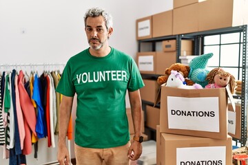 Middle age hispanic man wearing volunteer t shirt at donations stand looking sleepy and tired,...