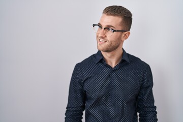 Fototapeta premium Young caucasian man standing over isolated background looking away to side with smile on face, natural expression. laughing confident.
