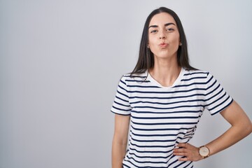 Obraz premium Young brunette woman wearing striped t shirt looking at the camera blowing a kiss on air being lovely and sexy. love expression.