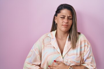 Blonde woman standing over pink background with hand on stomach because nausea, painful disease...