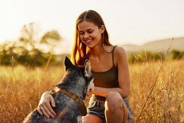 Woman smiling and stroking a husky dog ​​walking in nature in a field of grass in autumn