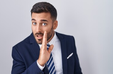 Handsome hispanic man wearing suit and tie hand on mouth telling secret rumor, whispering malicious talk conversation - obrazy, fototapety, plakaty