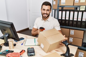 Young hispanic man smiling confident scanning package label with barcode reader at storehouse