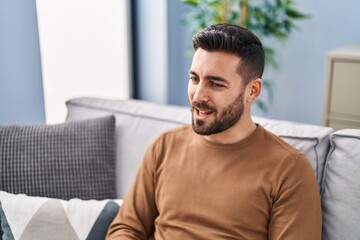 Young hispanic man sitting on sofa speaking at home