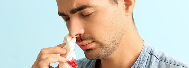 Young man with nosebleed on light blue background, closeup