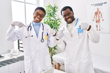 Young african american doctors working at medical clinic looking confident with smile on face, pointing oneself with fingers proud and happy.