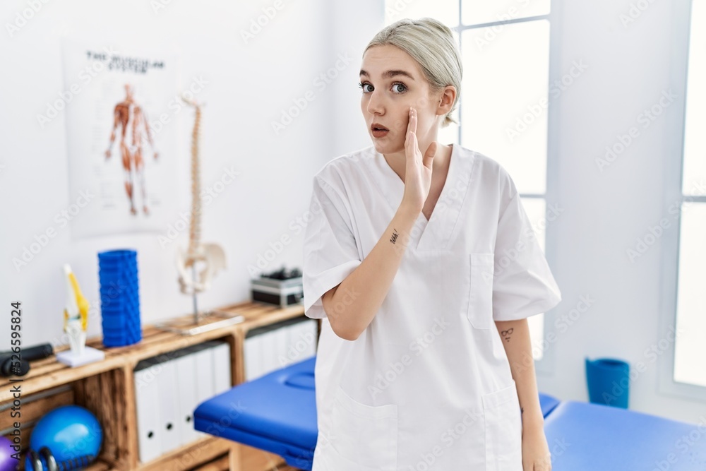 Sticker Young caucasian woman working at pain recovery clinic hand on mouth telling secret rumor, whispering malicious talk conversation