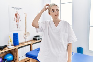 Young caucasian woman working at pain recovery clinic confuse and wondering about question. uncertain with doubt, thinking with hand on head. pensive concept.