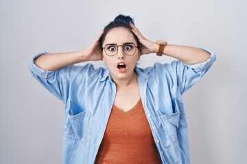 Young modern girl with blue hair standing over white background crazy and scared with hands on head, afraid and surprised of shock with open mouth