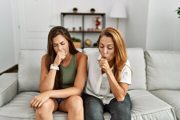 Mother and daughter together sitting on the sofa at home feeling unwell and coughing as symptom for cold or bronchitis. health care concept.