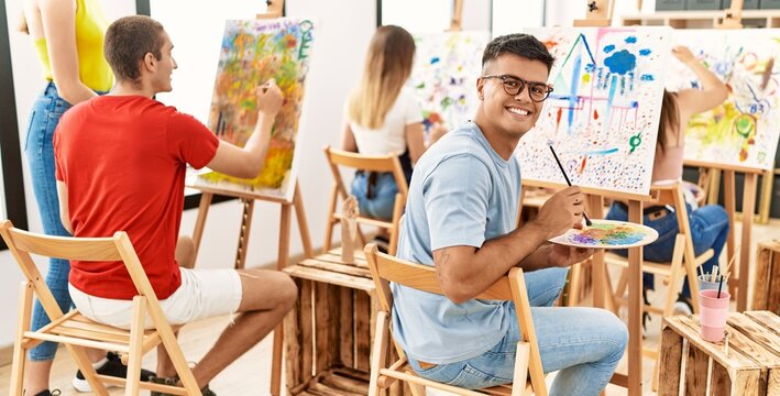 Young man smiling happy drawing with group of people at art studio.