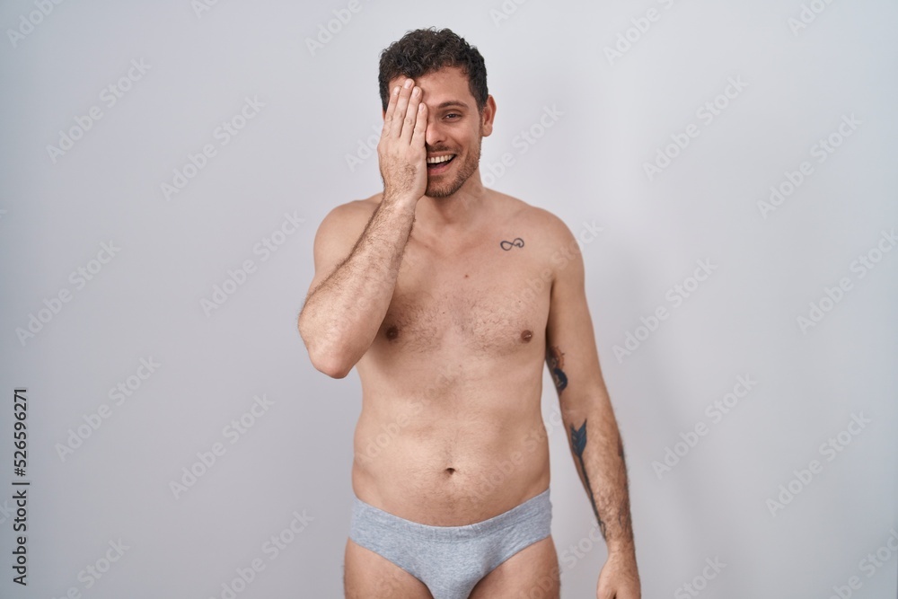 Canvas Prints Young hispanic man standing shirtless wearing underware covering one eye with hand, confident smile on face and surprise emotion.