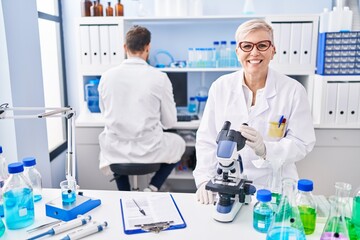 Middle age woman working at scientist laboratory looking positive and happy standing and smiling with a confident smile showing teeth