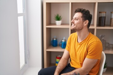 Young hispanic man smiling confident sitting on chair at home