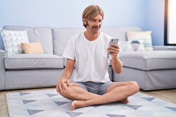 Young blond man smiling confident using smartphone at street