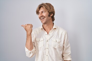 Middle age man standing over isolated background smiling with happy face looking and pointing to the side with thumb up.