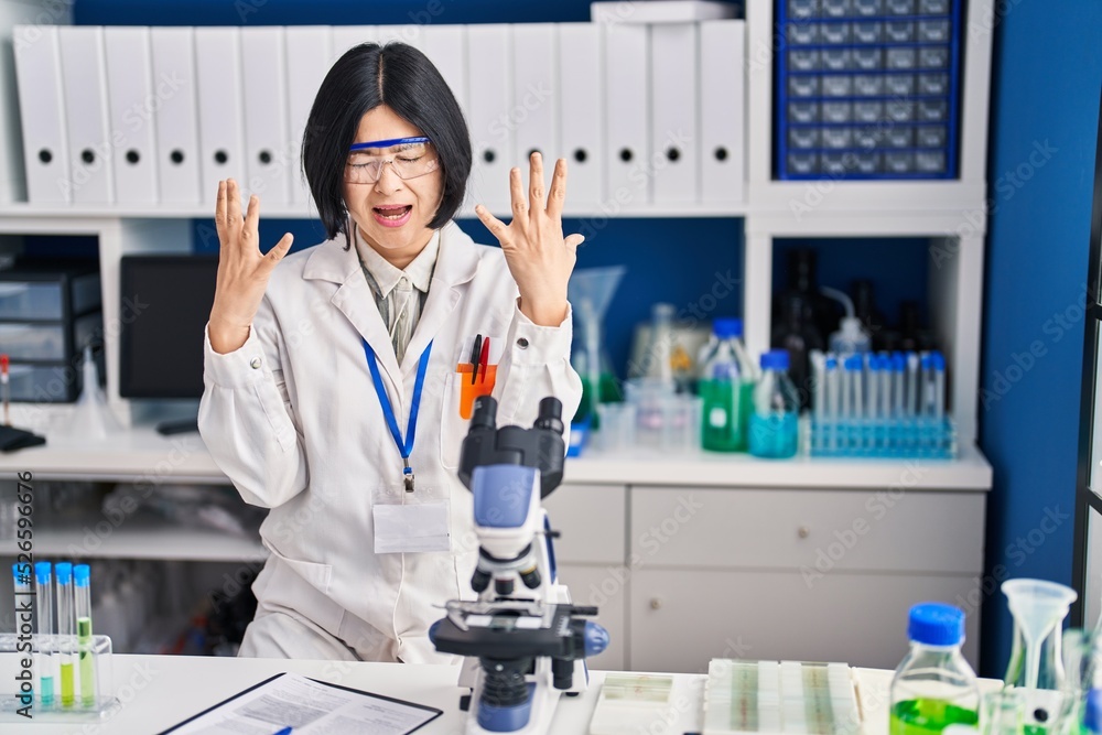 Sticker young asian woman working at scientist laboratory celebrating mad and crazy for success with arms ra