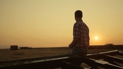 Farmer examining harvest on wheat field at golden sunset. Modern agro concept.