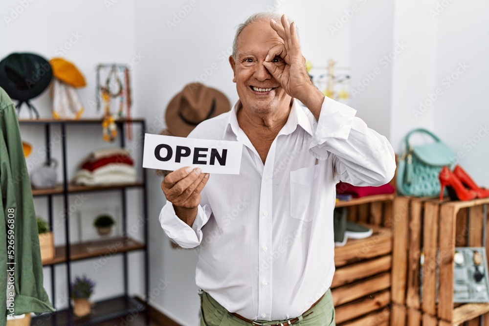 Sticker Senior man holding banner with open text at retail shop smiling happy doing ok sign with hand on eye looking through fingers