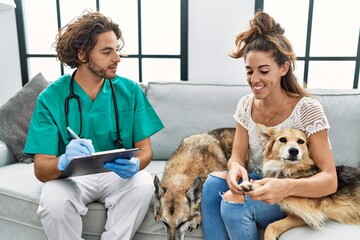 Man and woman wearing veterinarian uniform writing on clipboard at home