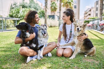 Man and woman couple smiling confident sitting on herb with dogs at park