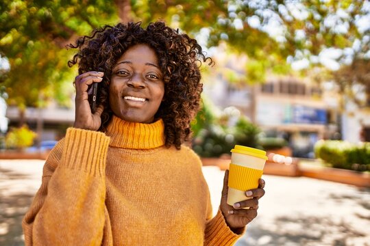African american woman talking on the smartphone drinking coffee at park