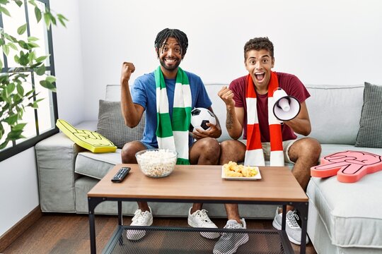 Young hispanic brothers football hooligans holding ball and megaphone screaming proud, celebrating victory and success very excited with raised arms