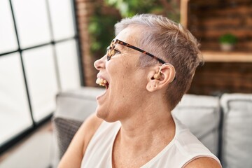 Middle age woman using hearing aid sitting on sofa at home